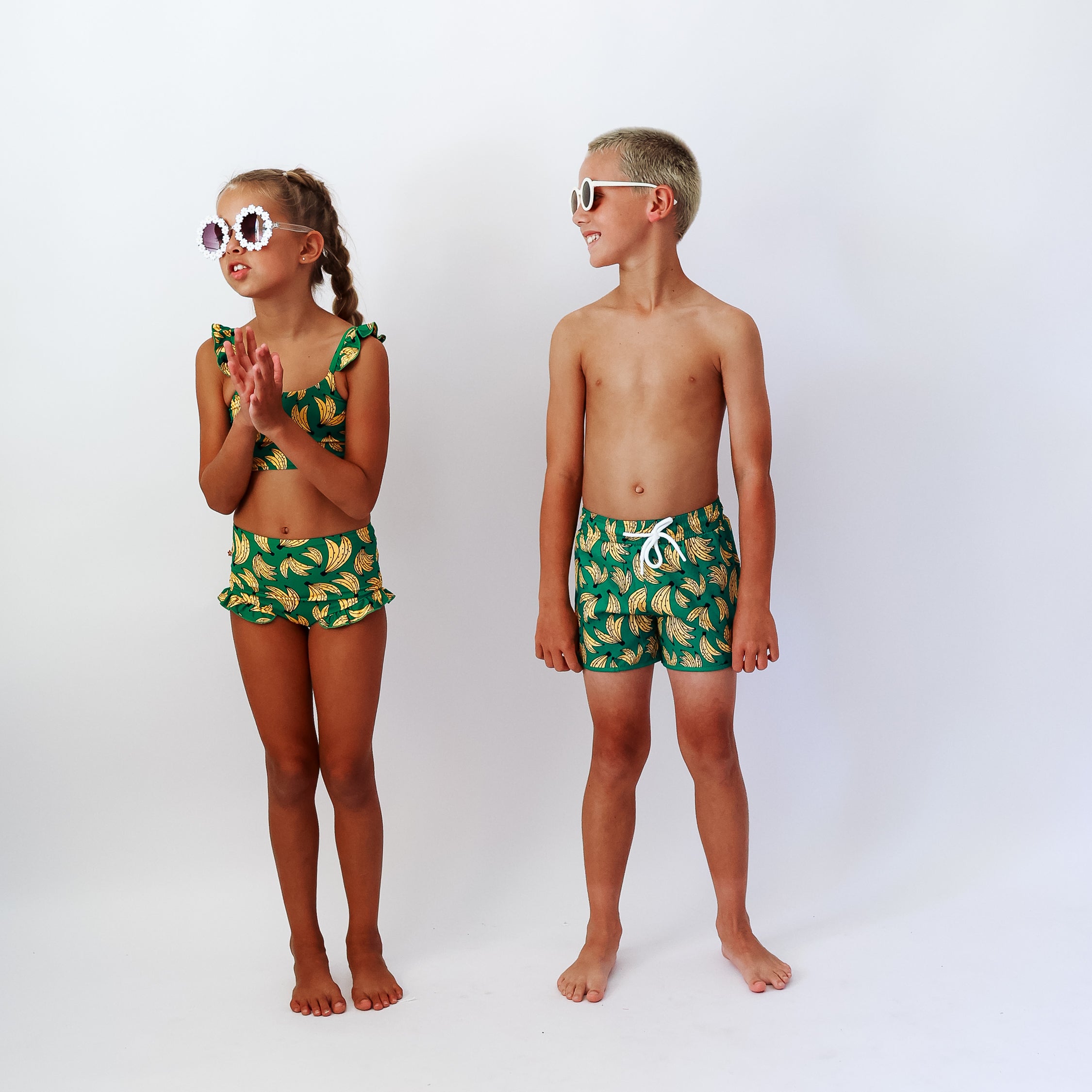 Two children wearing matching BANANA-patterned swimwear on a white background